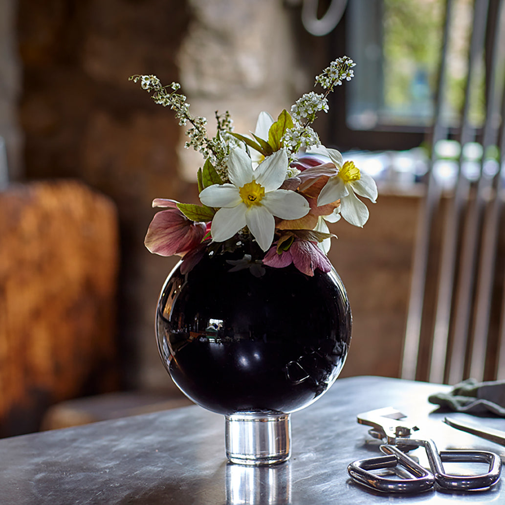 a round black glass vase filled with spring flowers