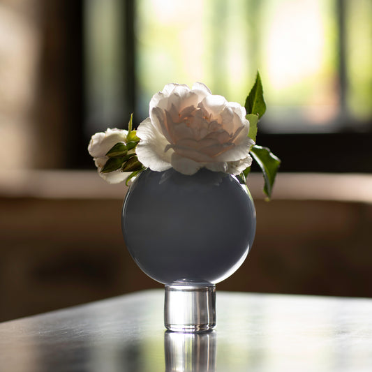A small grey ball vase with a flower on a table, capturing a moment of stillness and beauty.