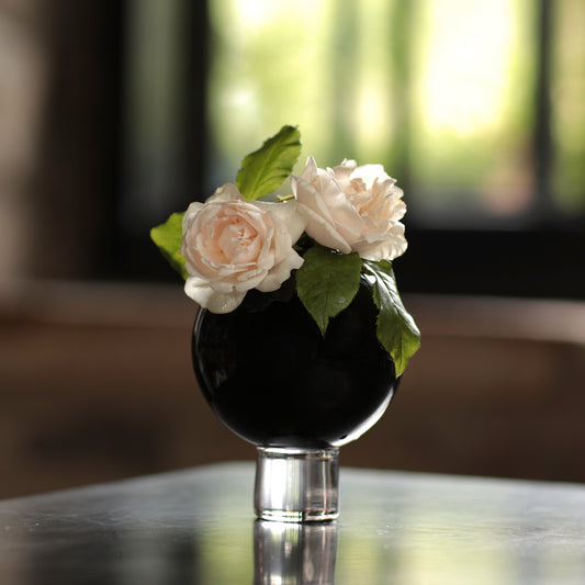 A small black ball vase on a table, filled with water and displaying a small bunch of pink roses.