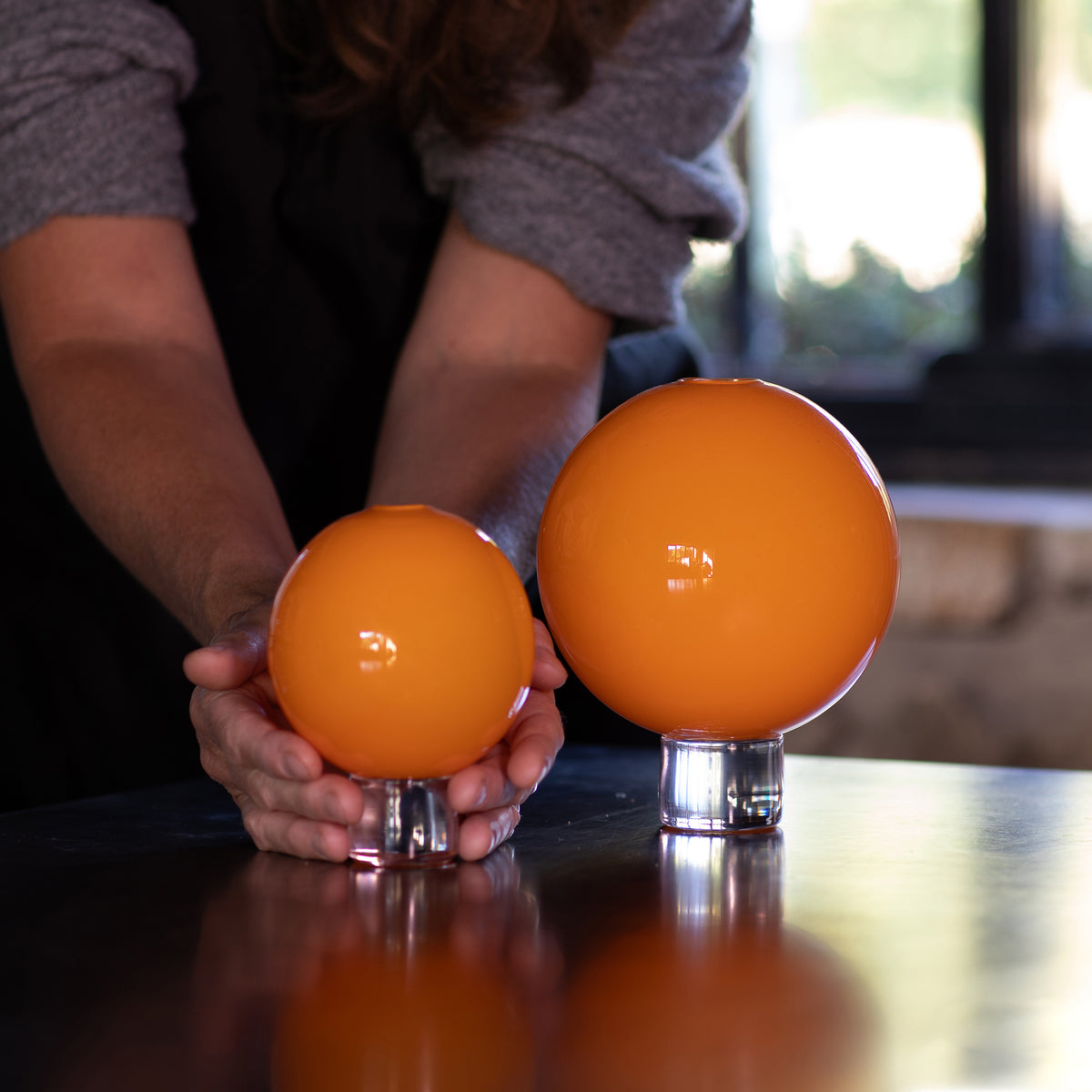 hand blown opaque orange glass vases with the makers hands for scale