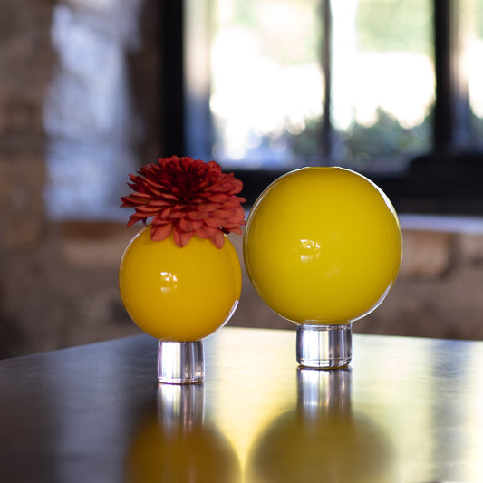 Two yellow glass round posey vases with one holding a red dahlia flower and the other empty