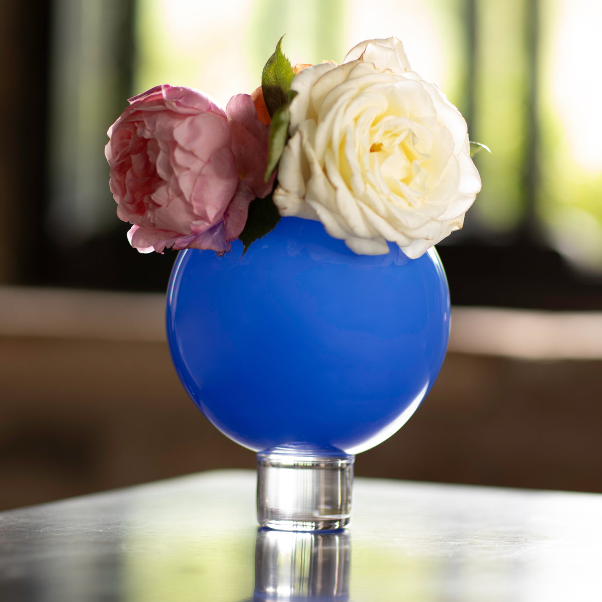 A large blue ball vase with a clear glass base, filled with pink and white flowers.